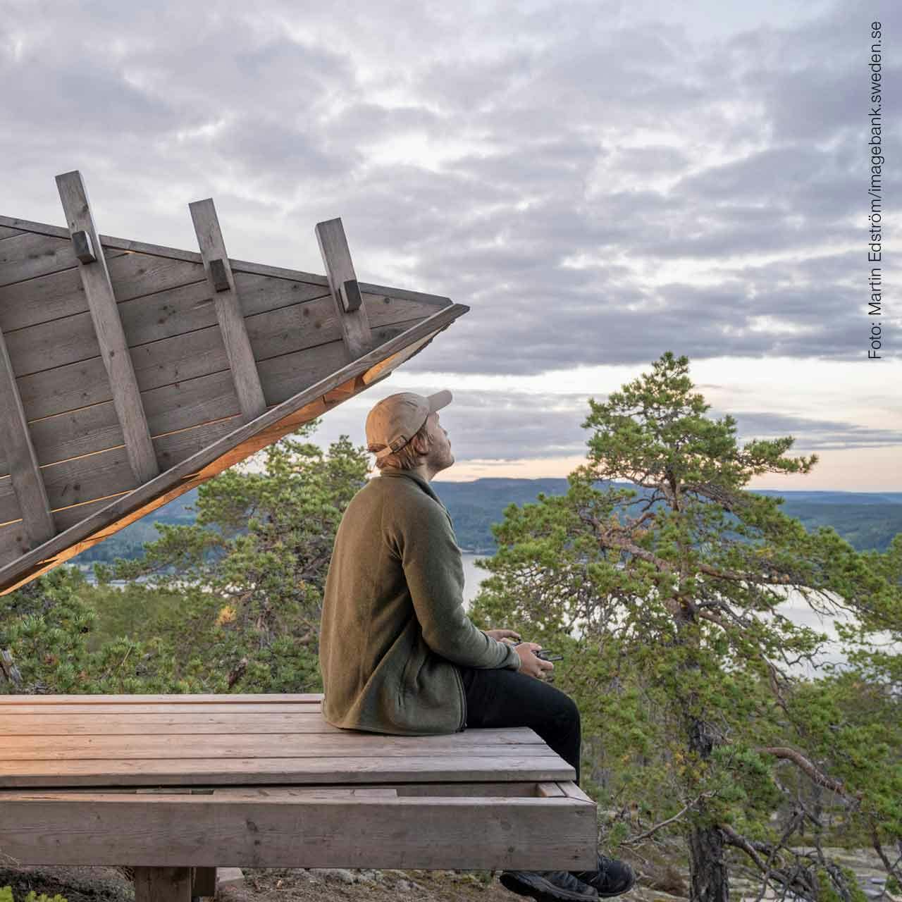 Man som sitter på ett trädäck  uppepå ett berg och blickar ut över Svenska fjäll